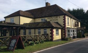 a yellow and white pub with a thatched roof , situated on the side of a country road at The Hunters Moon