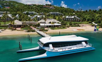 a white and blue boat is docked at a pier in a tropical location , surrounded by buildings and clear blue water at The Westin St. John Resort Villas