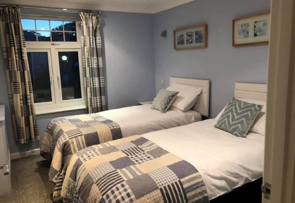 a bedroom with two beds , each made up with white sheets and blue - green checkered blankets , standing next to a window with blue curtains at Atlantic Lodge