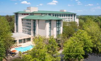 a large , modern hotel with a swimming pool and trees in the foreground , under a clear blue sky at Atlanta Marriott Alpharetta