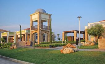 a large building with a dome and balcony is surrounded by green grass and rocks at Mediterranean Village Hotel & Spa