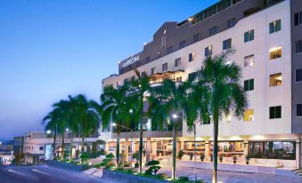 a large hotel with a restaurant located on the side of the street , surrounded by palm trees at Aston Karimun City Hotel