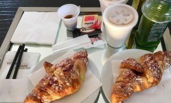 a dining table with a variety of pastries and beverages , including croissants , cups of coffee , and a plate of pastries at X Hotel