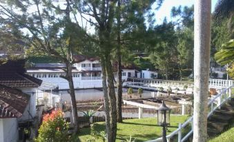 a house is situated next to a lake with trees and bushes surrounding it , under a clear blue sky at Marbella Twin Waterfall Resort Ciater