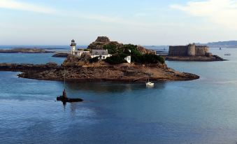 a small island with a lighthouse and a castle in the background , surrounded by water at Entre Terre et Mer