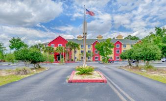 a red building with a flag on top is surrounded by palm trees and greenery at Magnuson Hotel Wildwood Inn Crawfordville