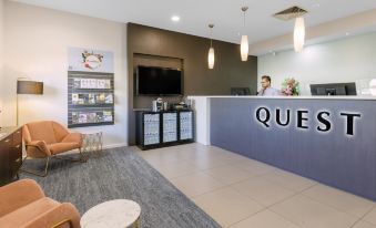 "a modern hotel lobby with a reception desk , seating area , and a tv screen , as well as a sign that reads "" queen ""." at Quest Werribee