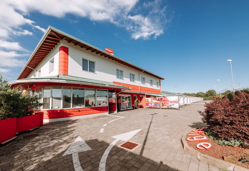 a red and white building with a red roof , located in a parking lot with cars parked outside at Hotel Motel Prestige