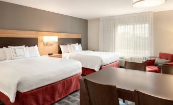 a hotel room with two beds , a dining table , and a window , all decorated in white and red at TownePlace Suites Milwaukee Grafton