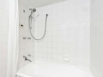 a white tiled bathroom with a bathtub , shower head , and faucet , as well as a window at Ibis Melbourne Hotel and Apartments