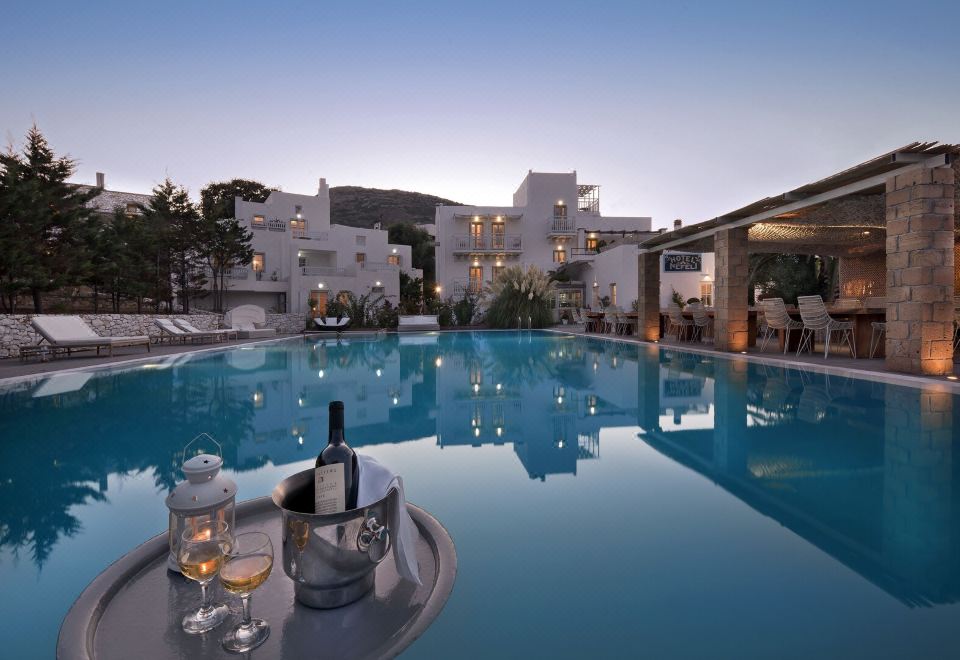 a beautiful outdoor pool area with a white building and clear blue water , surrounded by lush greenery at Hotel Nefeli