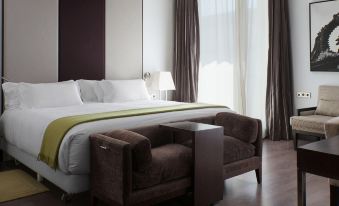 a modern hotel room with a large bed , white sheets , and a brown chair in the corner at NH Collection Santiago de Compostela