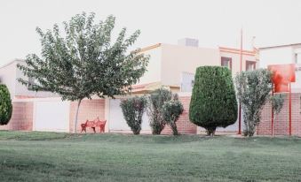 a lush green lawn with a red bench and a tree in front of a pink building at La Esperanza