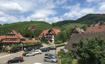 a picturesque village with houses , cars parked in the street , and green hills in the background at Hotel Restaurant der Engel, Sasbachwalden