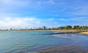 a beautiful beach with clear blue water and white sand , as well as a city skyline in the background at Carnegie Motor Inn