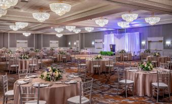 a large , well - decorated banquet hall with multiple round tables and chairs , creating an elegant atmosphere at Marriott Boston Quincy