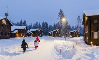 a group of people , including children and adults , are walking down a snowy path in front of a row of wooden cabins at Ranua Resort Holiday Villas