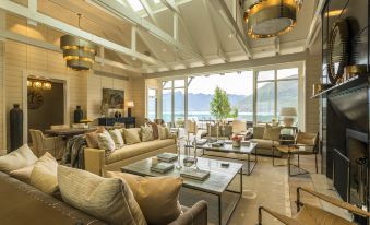 a large , elegant living room with multiple couches and chairs arranged around a coffee table , overlooking a beautiful view of the ocean at Rosewood Matakauri