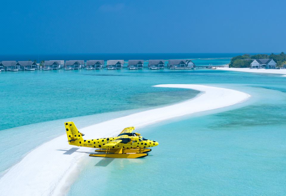 a yellow helicopter is parked on a sandy beach near a body of water , surrounded by palm trees at Four Seasons Resort Maldives at Landaa Giraavaru