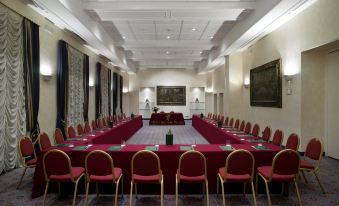 a large conference room with multiple long tables , each table covered in red tablecloths , and several chairs arranged around them at Sina Brufani