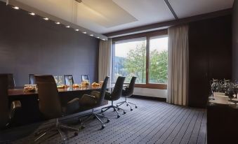 a modern office space with large windows , wooden floors , and comfortable seating arrangements , including black armchairs , white curtains , and natural light streaming at Kempinski Hotel Berchtesgaden