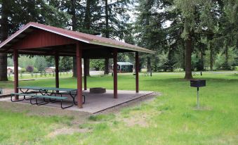 a covered picnic area in a wooded area , with a table and chairs set up for people to enjoy the outdoors at Lone Fir Resort