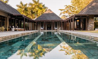 a large swimming pool with a reflection of the building in the water , surrounded by trees and a building with a thatched roof at Four Seasons Resort Mauritius at Anahita