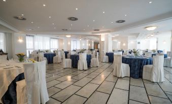 a large , empty banquet hall with white tables and blue tablecloths set up for an event at Hotel Capital