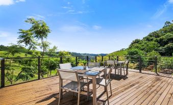 a wooden deck with a dining table and chairs set up for a meal , surrounded by lush greenery and a view of the countryside at Top of the Hill