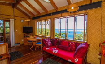 a cozy living room with a red couch , wooden floors , and large windows overlooking the ocean at 1770 Beach Shacks