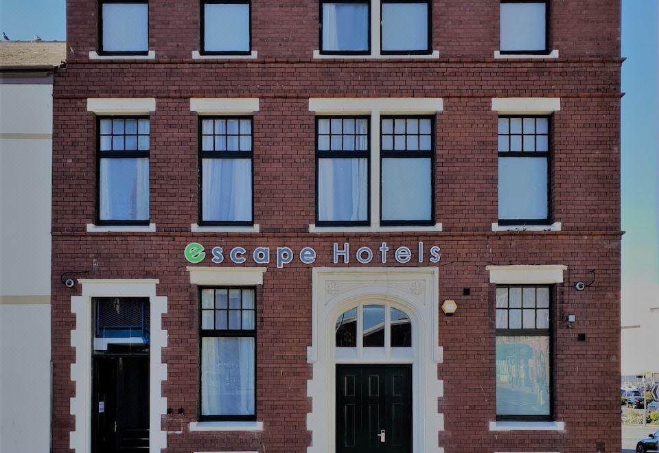 a brick building with multiple windows and doors , possibly a hotel or office building , located on a street corner at Escape Hotel