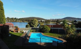 a beautiful swimming pool surrounded by lush greenery , with a clear blue sky and mountains in the background at Waterfront Lodge Motel