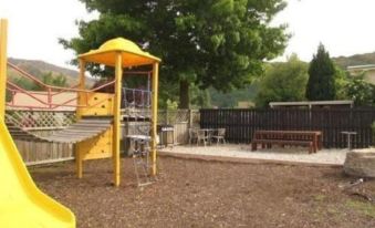 a playground with a yellow slide , swings , and other play equipment surrounded by a wooden fence at Arrowtown Motel