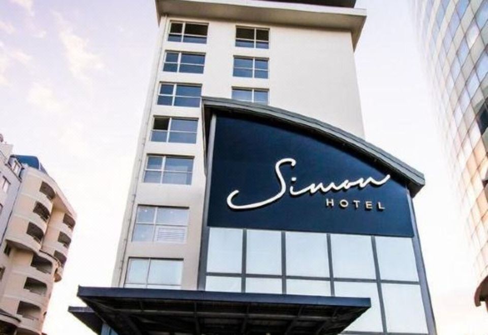 "a large hotel building with the name "" simon hotel "" displayed on its front , and it is surrounded by a crowd of people" at Simon Hotel