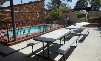 a courtyard with several picnic tables and benches , as well as a swimming pool nearby at Kallangur Motel