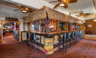 a bar with a thatched roof , surrounded by chairs and tables , in a restaurant setting at Best Western Dunmar Inn