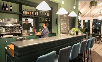 a modern bar with a green wall , wooden bar top , and various bottles on display at Ibis Nantes Saint-Herblain
