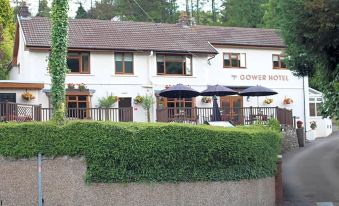 "a white building with a brown roof , two umbrellas on the front porch , and a stone wall , under which the word "" towers hotel """ at The Gower Hotel