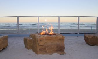 a stone fire pit on the beach , surrounded by sand and a view of the ocean at Lotus Boutique Inn and Suites
