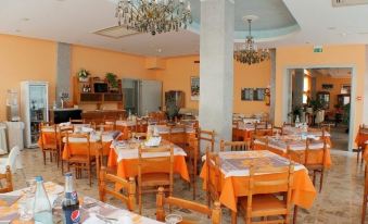 a well - lit dining room with multiple tables and chairs , some of which are covered in orange tablecloths at Hotel Jasmine