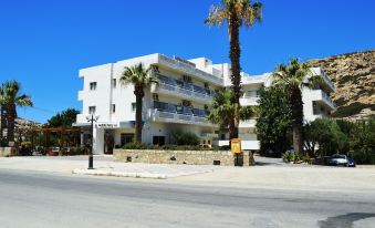 a white apartment building with palm trees in front of it , under a clear blue sky at Matala Bay Hotel & Apartments