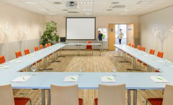 a conference room with a long table , chairs , and a projector screen , ready for a meeting or presentation at Ibis Styles Genève Carouge