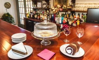 a cake stand with plates of food and glasses on a wooden bar , surrounded by bottles and other items at Rosewood Country Inn