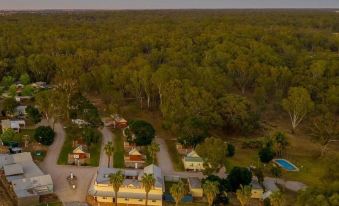 an aerial view of a forested area with a few houses and trees , along with a body of water in the background at Deniliquin Pioneer Tourist Park