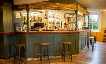 a bar with green walls and wooden chairs , featuring a large display of alcohol bottles behind the counter at Woodfalls Inn