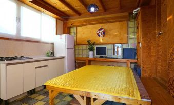 The kitchen is equipped with a table, refrigerator, and a bed in the center, all placed on top of an area rug at Jeonju Dwaejikkum Pension