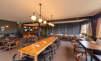 a modern restaurant with wooden tables and chairs , pendant lights , and a bar in the background at Great Lake Hotel