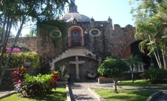 a stone church with a cross on the front , surrounded by green grass and trees at Hotel Hacienda Vista Hermosa