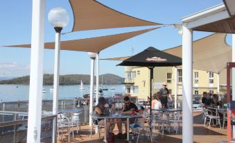 a group of people are sitting at tables under umbrellas on a deck overlooking the water at Beauty Point Waterfront Hotel