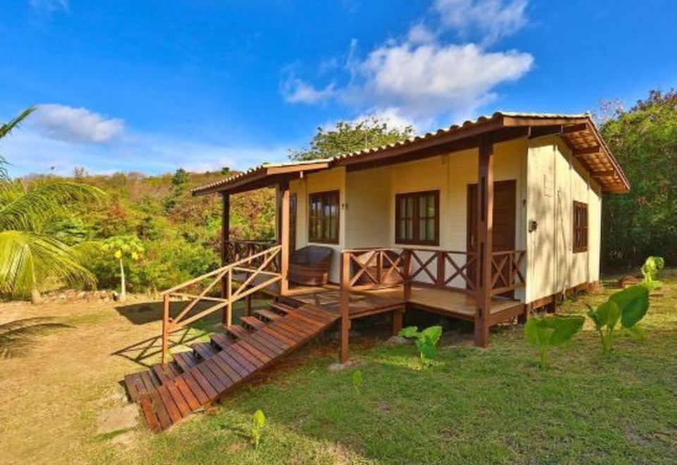 a small wooden house with a porch and steps leading up to it , situated in a lush green field at Pousada Simpatia da Ilha